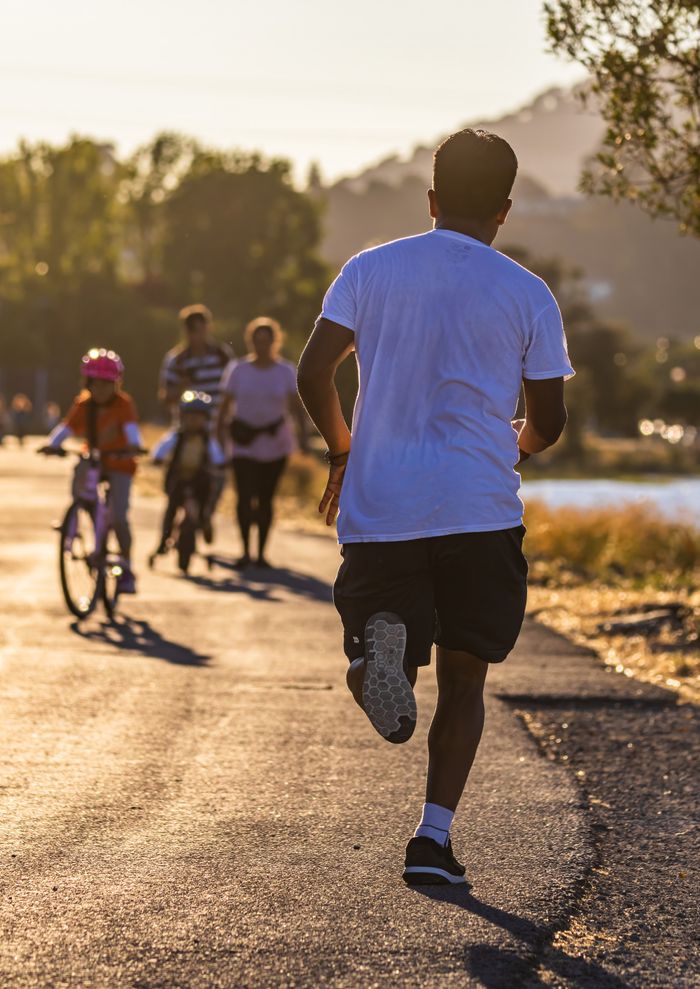 about-us-02 Man jogging along a scenic path at sunset with cyclists in the distance.